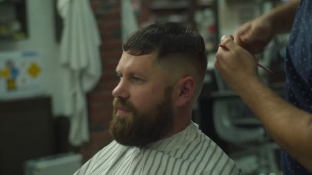 Mans hair cutting by barbers scissors and comb with barbershop logo behind in slow motion. Mans hands making male haircut in salon.  - Filmati, video