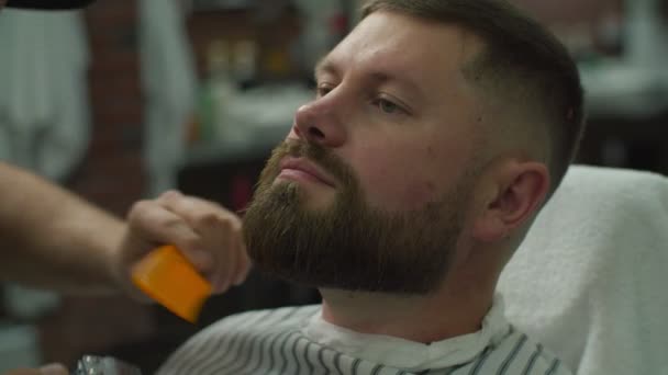 Bearded man and barbers hands shaving beard by electric shaving machine and comb in slow motion. Male with closed eyes in barbershop.  - Video, Çekim
