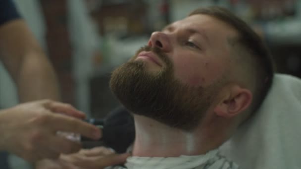 Barber hand applying talc on mans face with beard by barbers brush in slow motion.  - Záběry, video