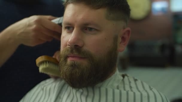 Barbers hand shaving mans head by electric shaving machine, front view in slow motion. Man with beard in barbershop - Filmmaterial, Video
