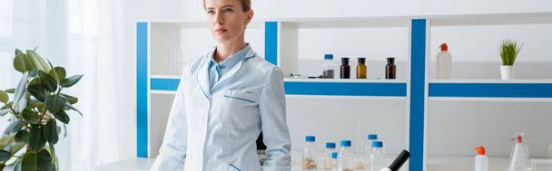 panoramic shot of biologist in white coat looking away in lab  - Foto, Bild