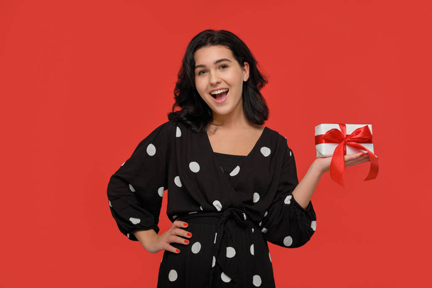 Bruna donna in un abito nero sorridente in possesso di regalo di Natale scatola di colore bianco con nastro rosso
. - Foto, immagini