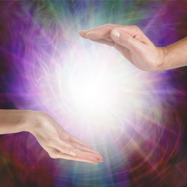 Together our healing energies combine to create a powerful influence - male hand opposite female hand with a white light orb in between against a multicoloured flowing energy field background with copy space - Photo, Image