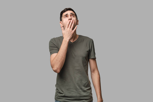 Young brunet man yawning isolated over grey background. Being tired after long working day. - Foto, Imagen
