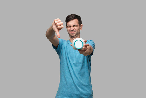 Young brunet man showing thumb down holding alarm isolated over grey background. - Photo, Image