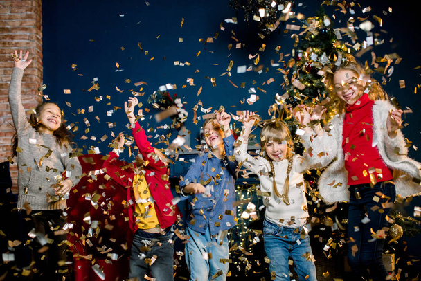 Los niños encantadores y hermosos que juegan con los confeti durante la fiesta sobre el fondo de las decoraciones navideñas. Concepto de invierno y año nuevo
. - Foto, Imagen