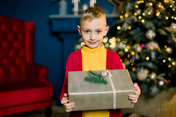 Little boy smiles and holds a Christmas present on the eve of the holidays. - Foto, imagen