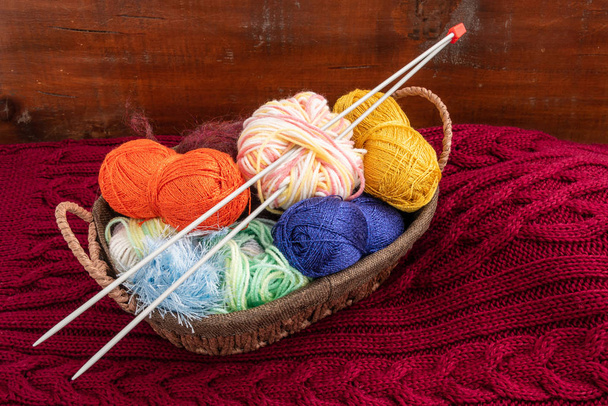 Des écheveaux de fils pour tricoter se trouvent dans un panier. Le panier est sur un tissu tricoté
. - Photo, image