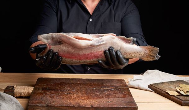 chef in a black shirt and black latex gloves holds a raw carcass - Foto, afbeelding