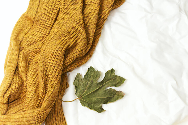 μάλλινο κασκόλ και φύλλα στο κρεβάτι, γεια έννοια χειμώνα - Φωτογραφία, εικόνα