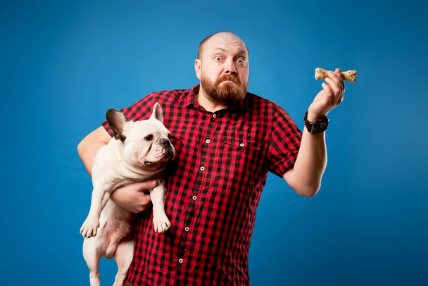 Man in shirt holds dog and bone on empty blue background - Foto, imagen