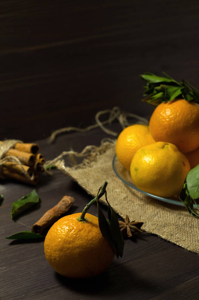 mandarina saborosa em primeiro plano. frutas maduras na mesa. tangerinas laranja fresca com folhas verdes em uma placa de vidro em um fundo de madeira escura. Chave baixa. vertical
 - Foto, Imagem
