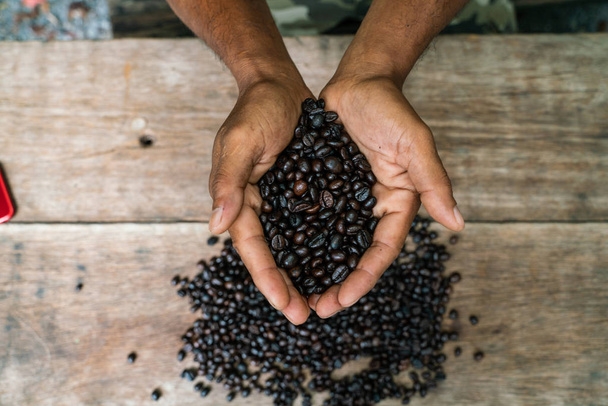Roasted arabica coffee bean in hand on wooden table - Zdjęcie, obraz