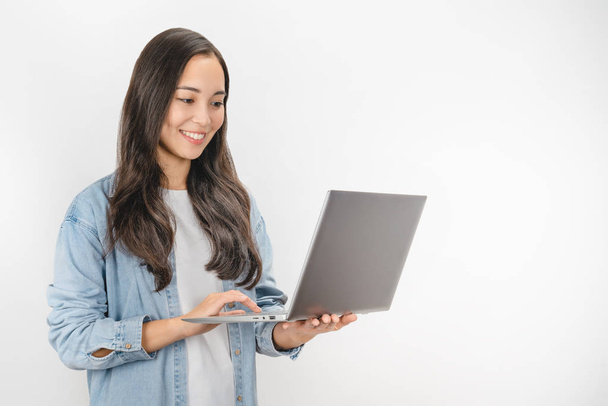 Молода щаслива усміхнена жінка в повсякденному одязі тримає ноутбук і надсилає електронну пошту, стоячи на білому тлі
 - Фото, зображення