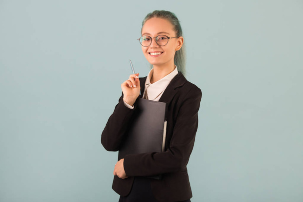 beautiful young woman in glasses and a black suit on a blue background with a folder in her hands - Фото, зображення