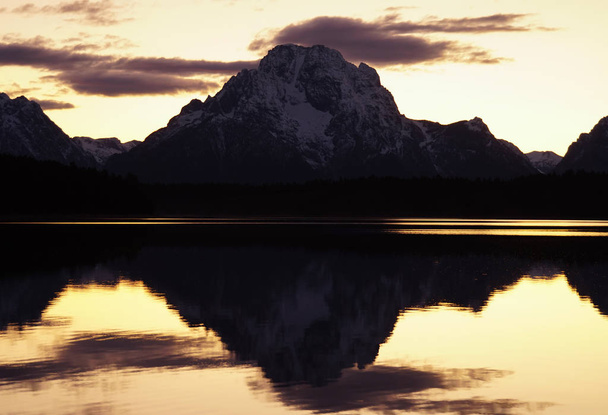 Het stille meer weerspiegelt de berg perfect op de achtergrond in het afnemende licht na zonsondergang. - Foto, afbeelding