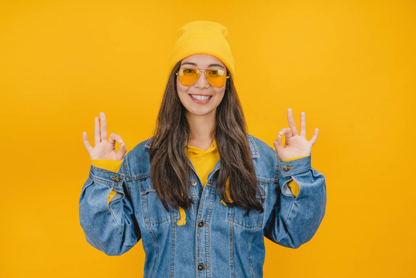 Happy young woman showing ok sign with fingers isolated on yellow background - Foto, imagen