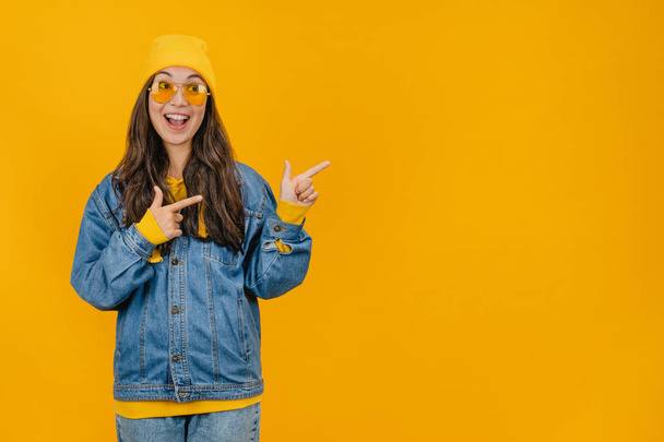 Happy young lady standing isolated over yellow background and pointing on copy space - Photo, Image