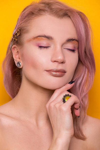 Shiny golden make-up on a beautiful young European model girl isolated on an orange background in the photo studio - Φωτογραφία, εικόνα