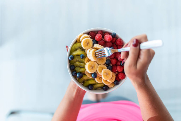 Woman's hands holding a bowl with fresh fruit while standing at home. - Photo, Image