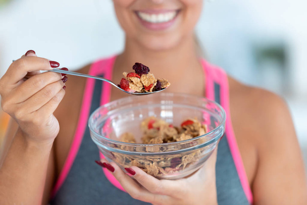 Smiling young woman eating cereals with strawberries at home. - Photo, Image