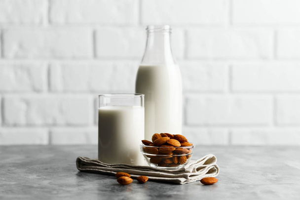 Glass reusable bottle and mug with almond milk and almonds on a marble countertop, kitchen with a white brick wall. - Fotó, kép