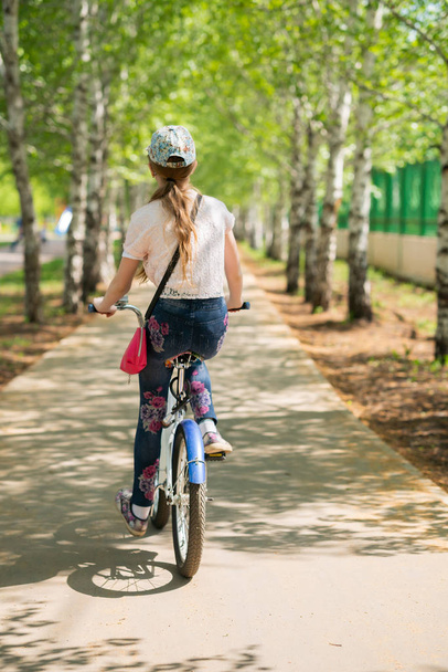 Girl on a bicycle rides on a bike path in the park. Cyclist in the park, back to camera. - Fotó, kép
