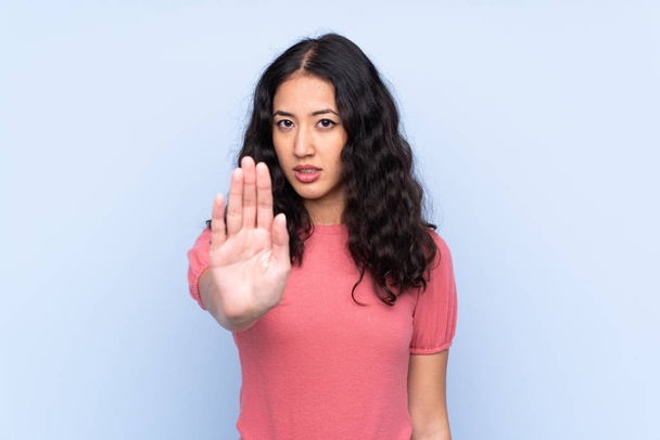 Mixed Race Frau trägt einen Pullover über isoliertem blauem Hintergrund macht Stop-Geste mit der Hand - Foto, Bild