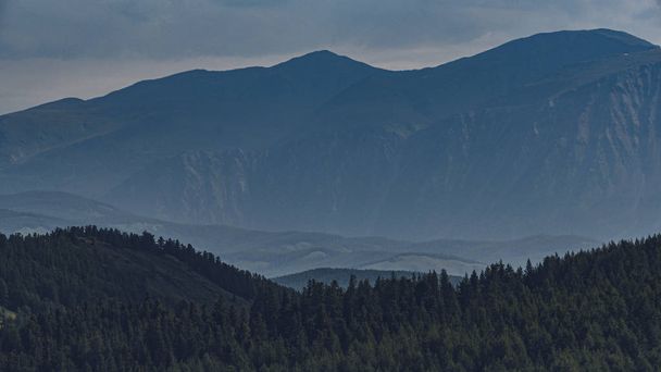 Λόφοι σε μπλε ομίχλη στον ορίζοντα. Σιλουέτες των βουνών στην κοιλάδα το ηλιοβασίλεμα - Φωτογραφία, εικόνα
