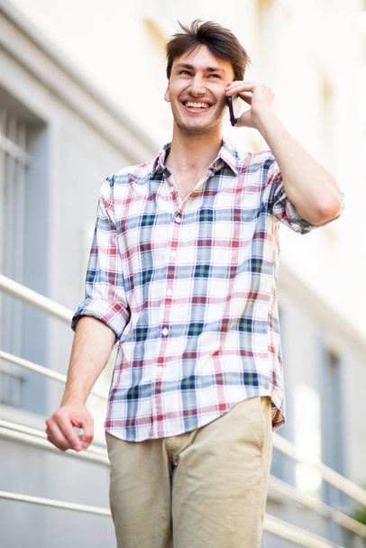 Portret van een knappe jongeman die loopt en praat met een mobiele telefoon in de stad - Foto, afbeelding