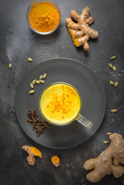 Cup of ayurvedic golden turmeric latte milk with curcuma powder and anise star on black. View from above. - Foto, Imagem