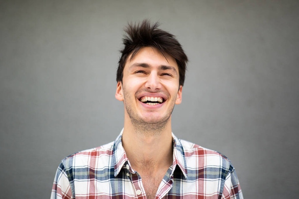 Detailní záběr portrét šťastný mladý muž smějící se na šedém pozadí a vzhlíží - Fotografie, Obrázek