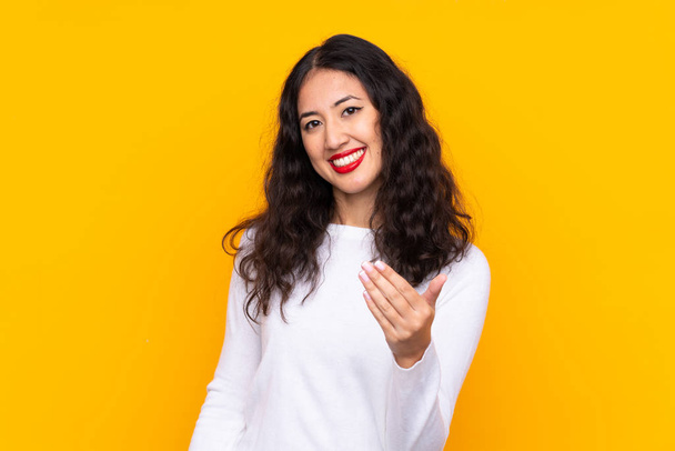 Mixed race woman over isolated yellow background inviting to come - Valokuva, kuva