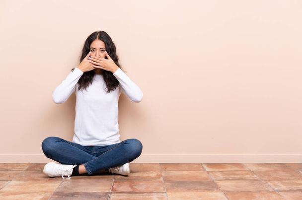 Young woman sitting on the floor covering mouth with hands - Photo, Image