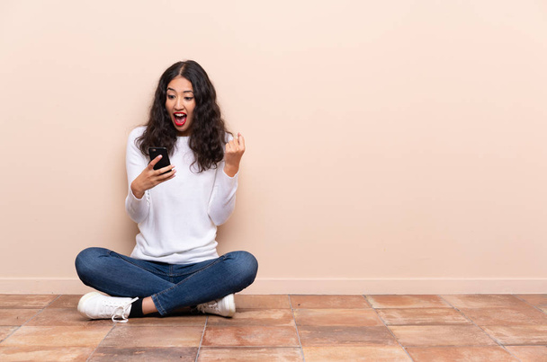 Jeune femme assise par terre surprise et envoyant un message - Photo, image