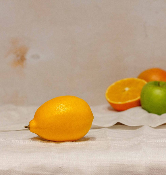 один желтый лимон на белой льняной скатерти и другие свежие фрукты на заднем плане
 - Фото, изображение