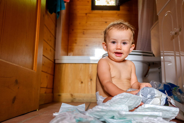 Baby op de vloer van de badkamer maken een puinhoop met zijn luiers - Foto, afbeelding
