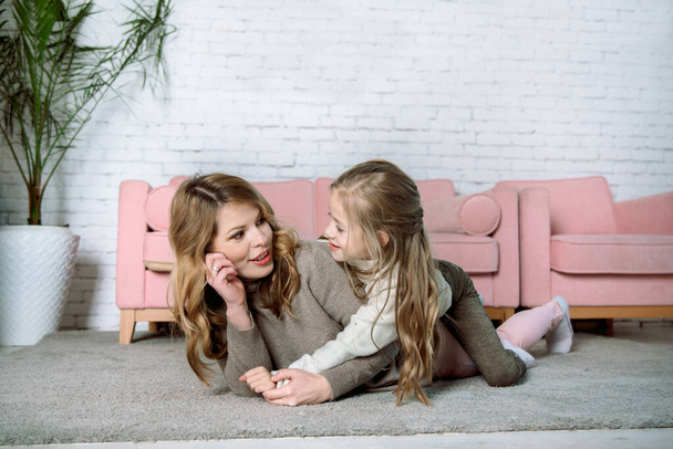 young woman and little daughter .The houses lie on the floor near the sofa, hugging and laughing, caring and tenderness. mother's love. Kiss, tenderness and care of mom.The concept parenting - Photo, Image