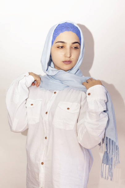 Elegantní muslimka v bílé košili a jasně modrém hidžábu. Stylová íránská dívka v muslimském oblečení. Izolovaný portrét atraktivní středovýchodní ženy - Fotografie, Obrázek
