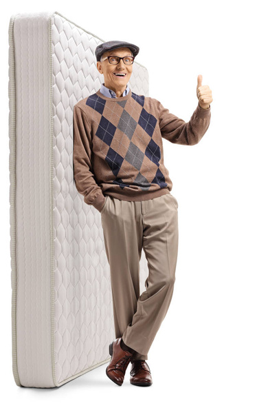 Happy senior gentleman leaning on a mattress and gesturing a thu - 写真・画像
