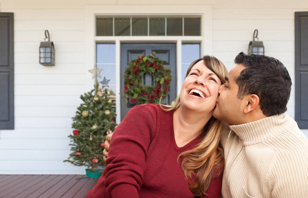 Pareja de adultos jóvenes hispanos y caucásicos en el porche de la casa decorado en Navidad
 - Foto, Imagen