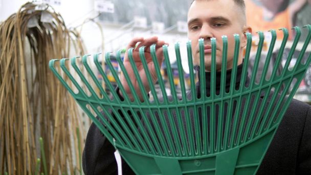 a young man chooses in store a rake for harvesting grass and leaves - Foto, Bild