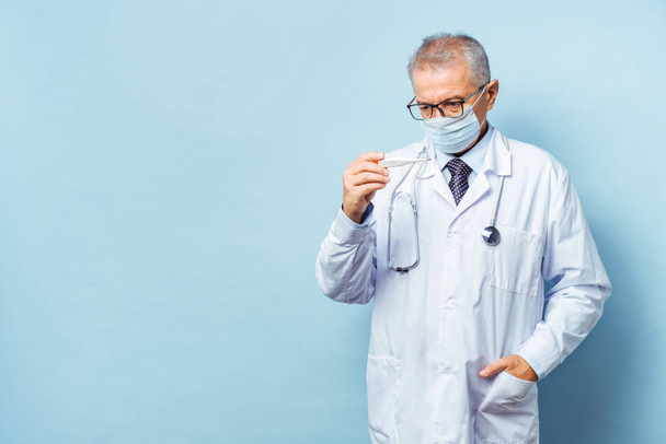 Portrait of a handsome senior doctor holding a thermometer in his hands, on a thermometer, the normal temperature of a healthy person is 36.6 degrees Celsius. Healthcare concept, flu prevention. - Photo, Image