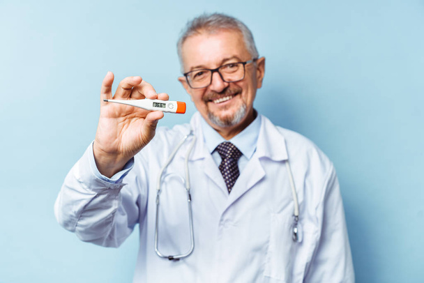 Porträt eines gut aussehenden Oberarztes, der ein Thermometer in der Hand hält, auf einem Thermometer liegt die normale Temperatur eines gesunden Menschen bei 36,6 Grad Celsius. Gesundheitskonzept, Grippeprävention. - Foto, Bild