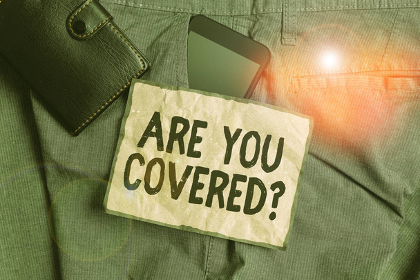 Conceptual hand writing showing Are You Covered Question. Business photo showcasing asking showing if they had insurance in work or life Smartphone device inside trousers front pocket with wallet. - Photo, Image