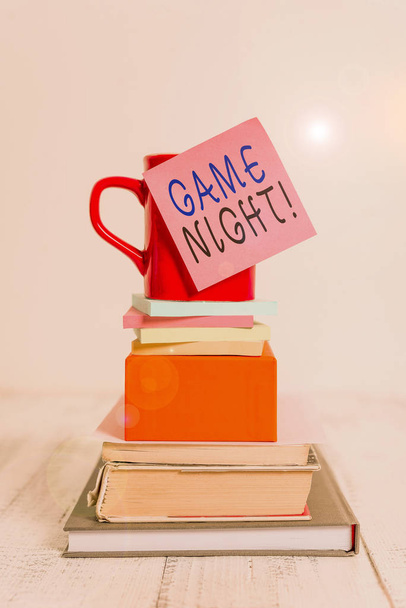 Conceptual hand writing showing Game Night. Business photo showcasing usually its called on adult play dates like poker with friends Cup sticky note stacked note pads books box wooden table. - Photo, Image
