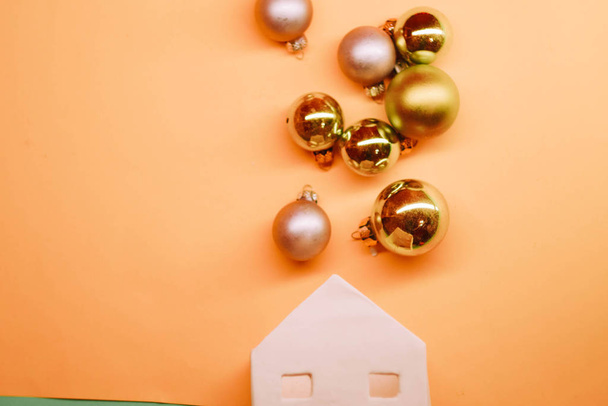 White toy house with golden Christmas balls. Pastel lush lava background. Copy space. Celebrating New Year - Photo, Image