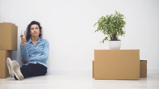 Young lady is sitting on the floor. There is a lot nude boxes and a plant near her. Copy space. 4K. - Footage, Video