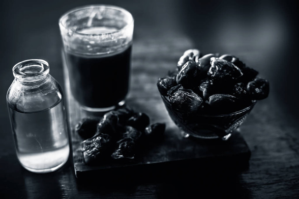 Dates syrup in a glass along with some raw dried dates and some cooking oil in a glass bottle on a wooden surface.Horizontal shot of date syrup with raw dried dates and cooking oil. - Photo, Image