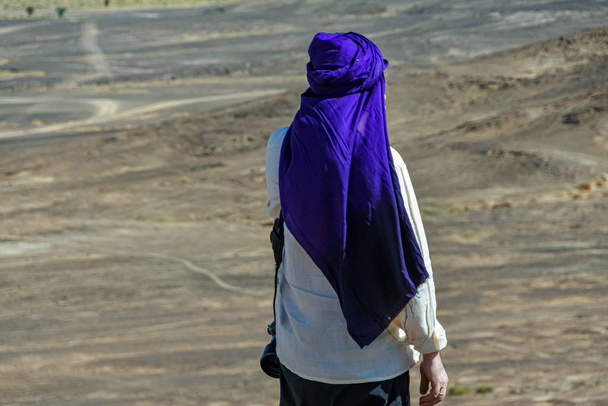 Πορτρέτο του άνδρα με λευκό πουκάμισο και μπλε τουρμπάνι στην πλάτη του στην έρημο του Μαρόκου - Φωτογραφία, εικόνα